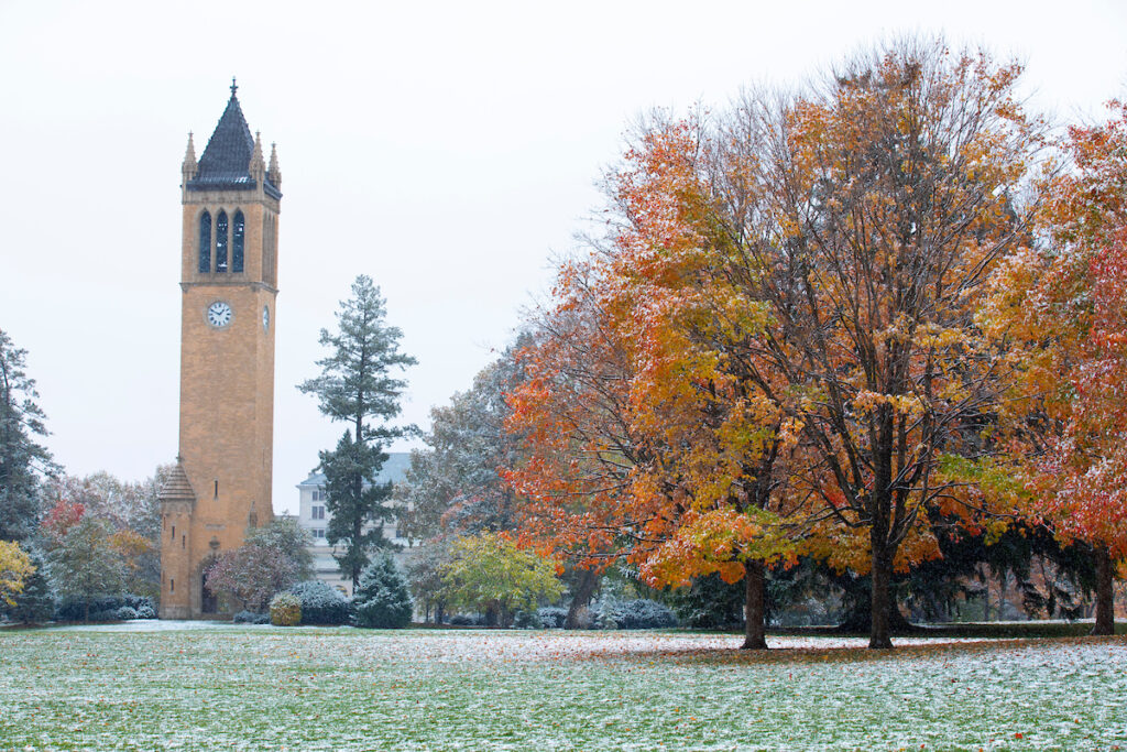 Iowa State campanile in the early stages of winter. The clock tower is feature with some trees and a light dusting of snow.